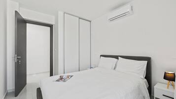 A modern hotel room with a bed, a nightstand, a lamp, and an air conditioning unit.