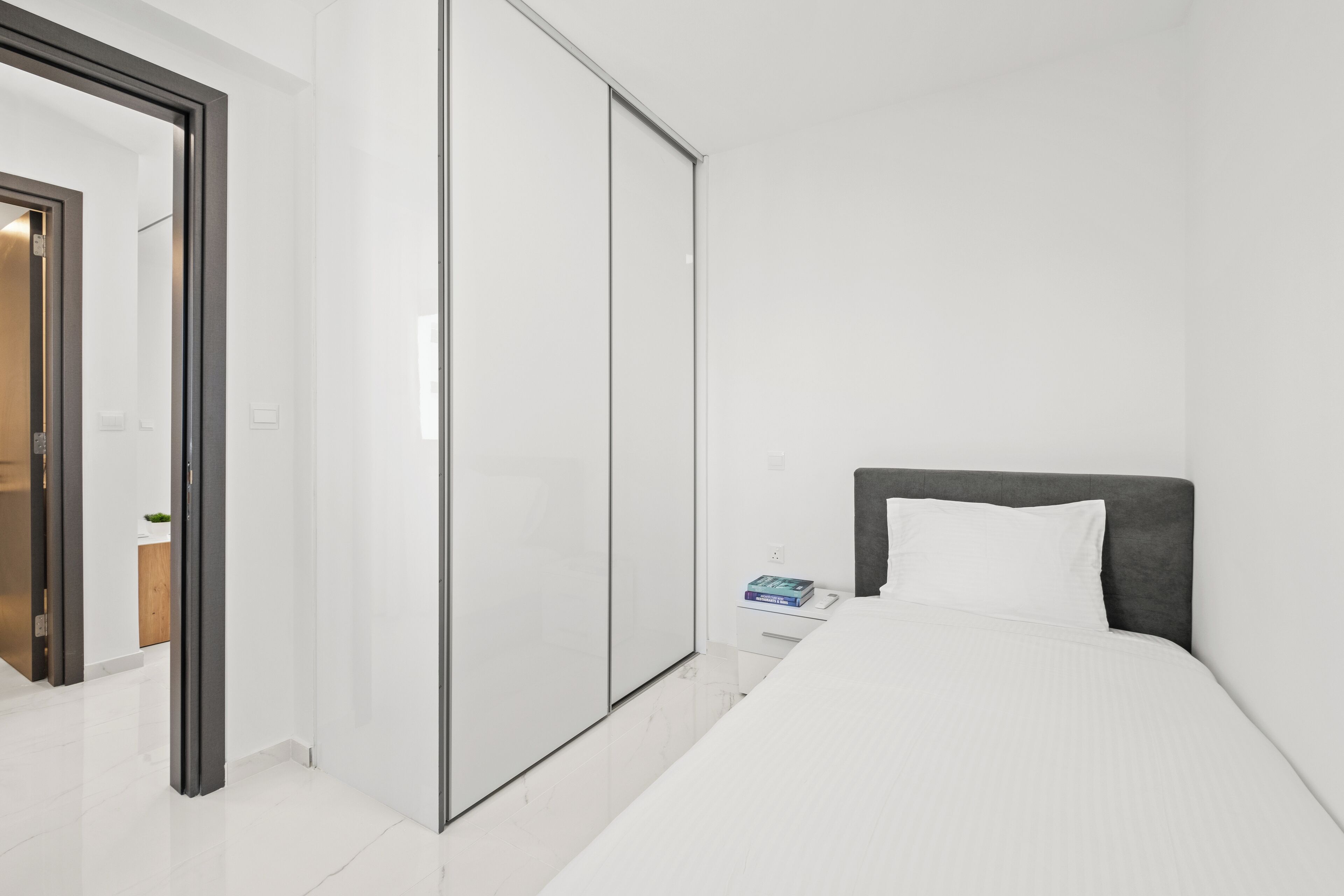 A modern hotel room with a large bed, a wardrobe, and a small bedside table.