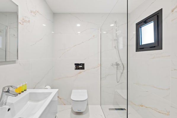 A modern bathroom with a white marble wall, a glass shower enclosure, a white toilet, and a built-in window. - Maestro City Apartments (Larnaca)