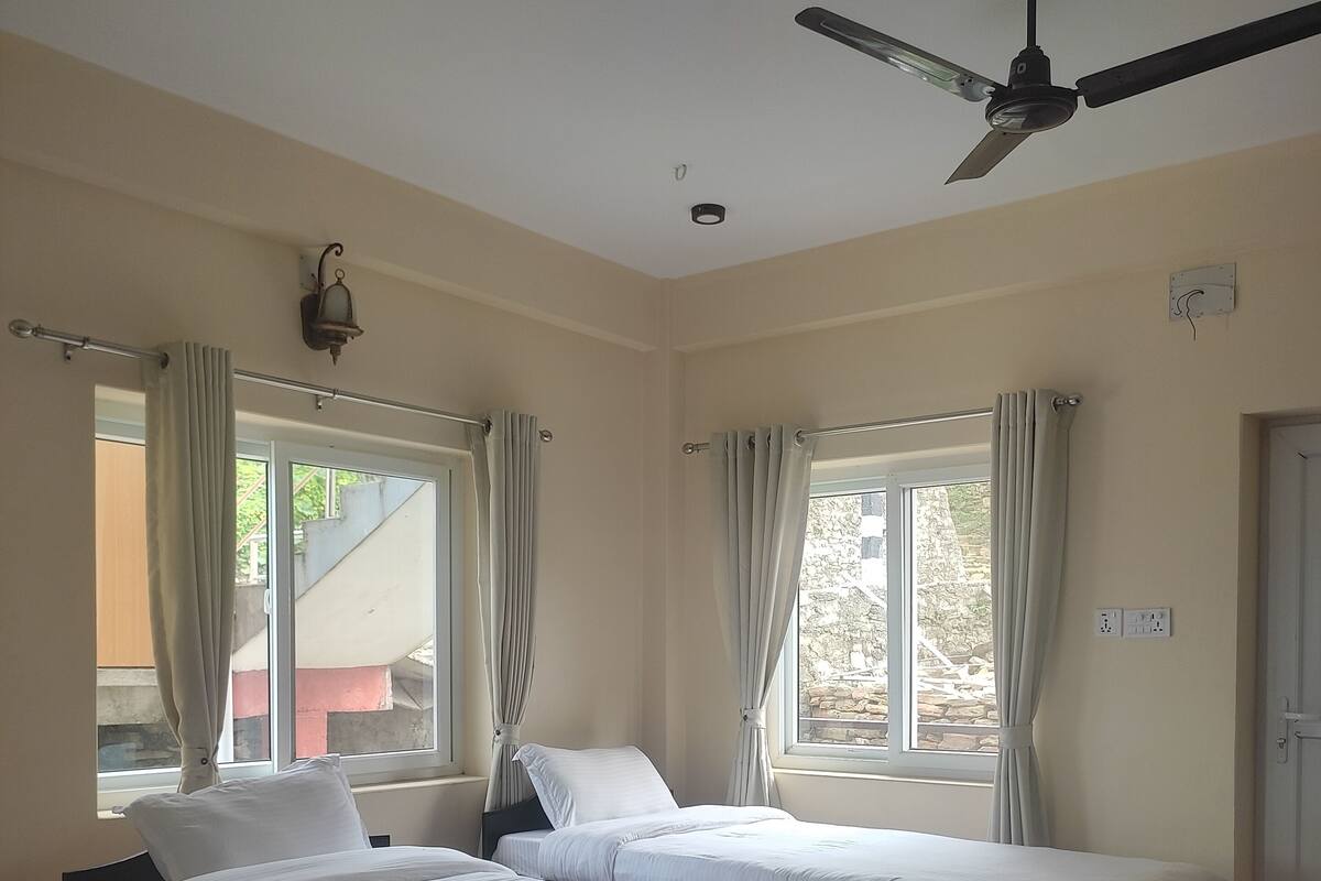 A hotel room with three beds, a ceiling fan, and large windows with curtains.