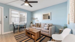Ein Wohnzimmer mit Deckenventilator, einer Couch, einem Couchtisch, einem Esstisch mit Stühlen und einem kleinen Beistelltisch.