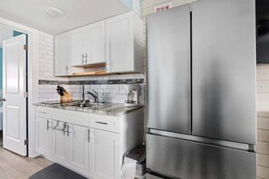 A modern kitchen with white cabinets, a stainless steel refrigerator, and a marble countertop.