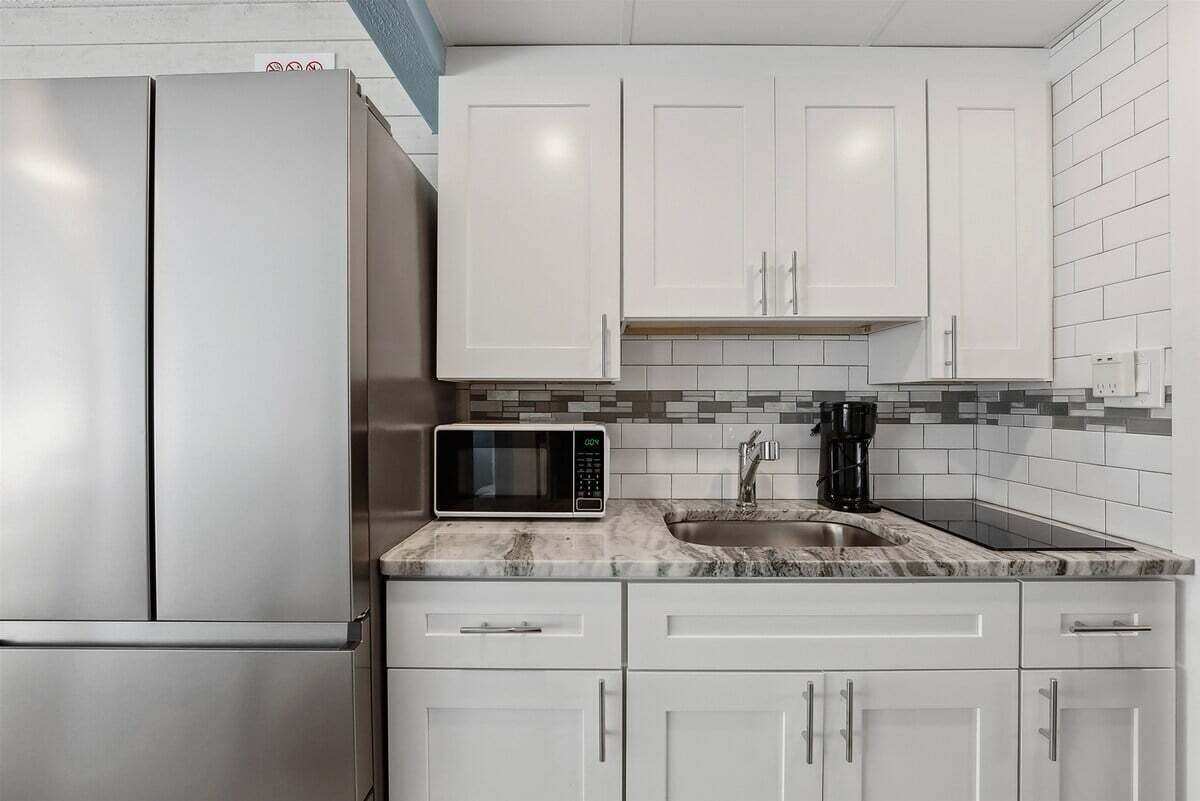 A kitchen with white cabinets, a stainless steel refrigerator, a microwave, and a coffee maker on the countertop.