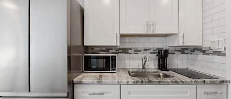 A kitchen with white cabinets, a stainless steel refrigerator, a microwave, and a coffee maker on the countertop.