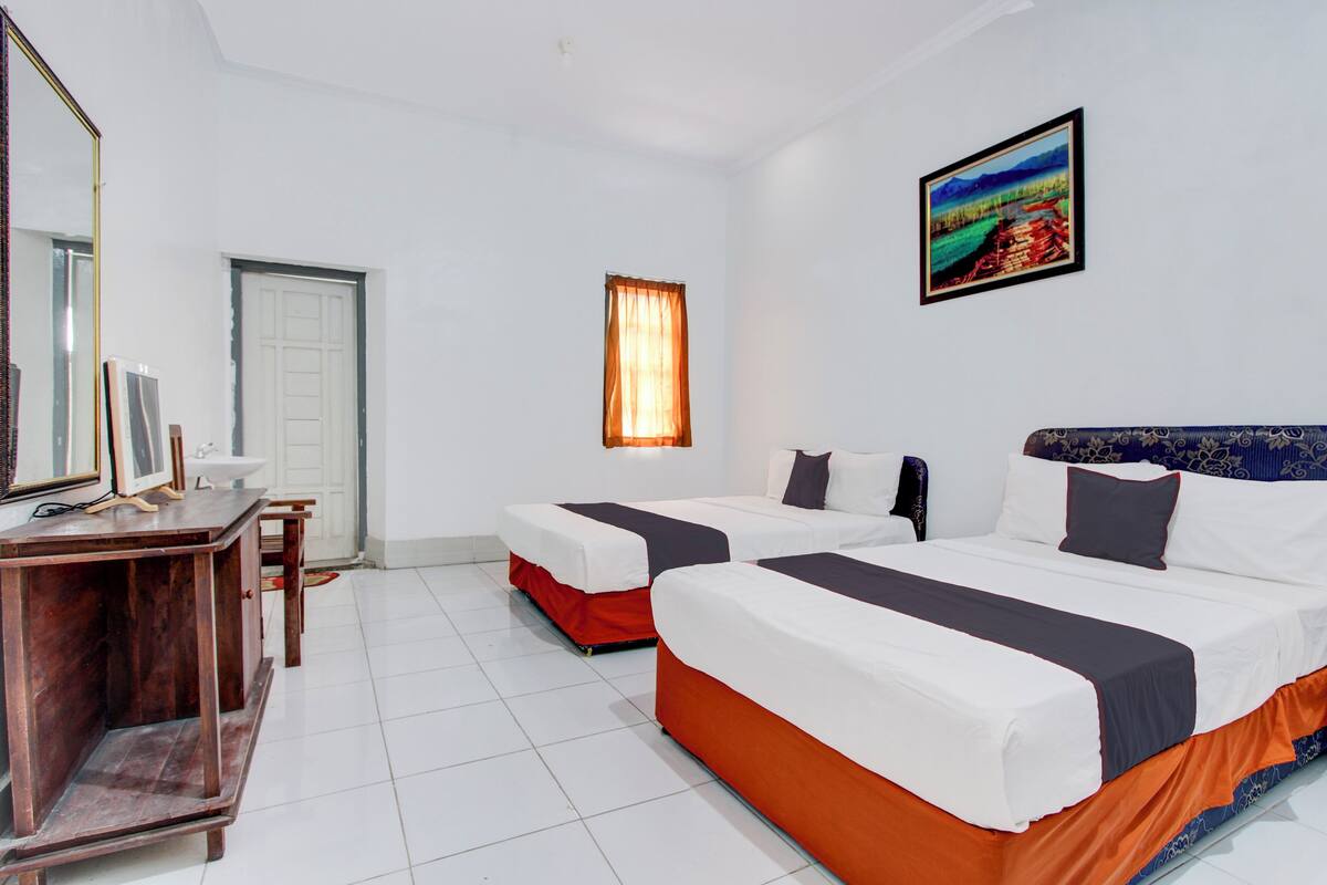 A hotel room with two beds, a desk, a mirror, and a window with curtains.