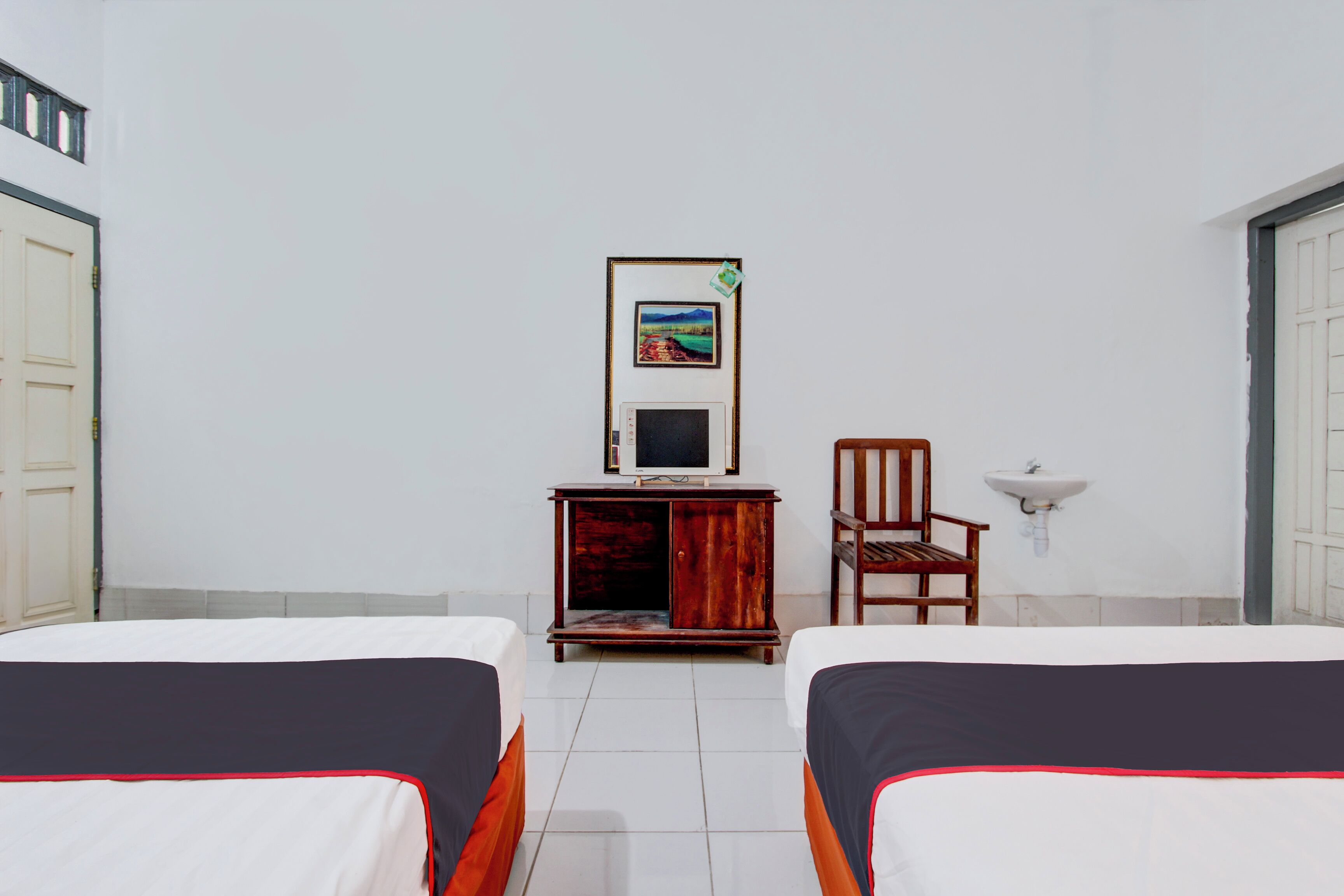 Une chambre d’hôtel avec deux lits, une armoire en bois avec un téléviseur, une chaise et un lavabo fixé au mur.