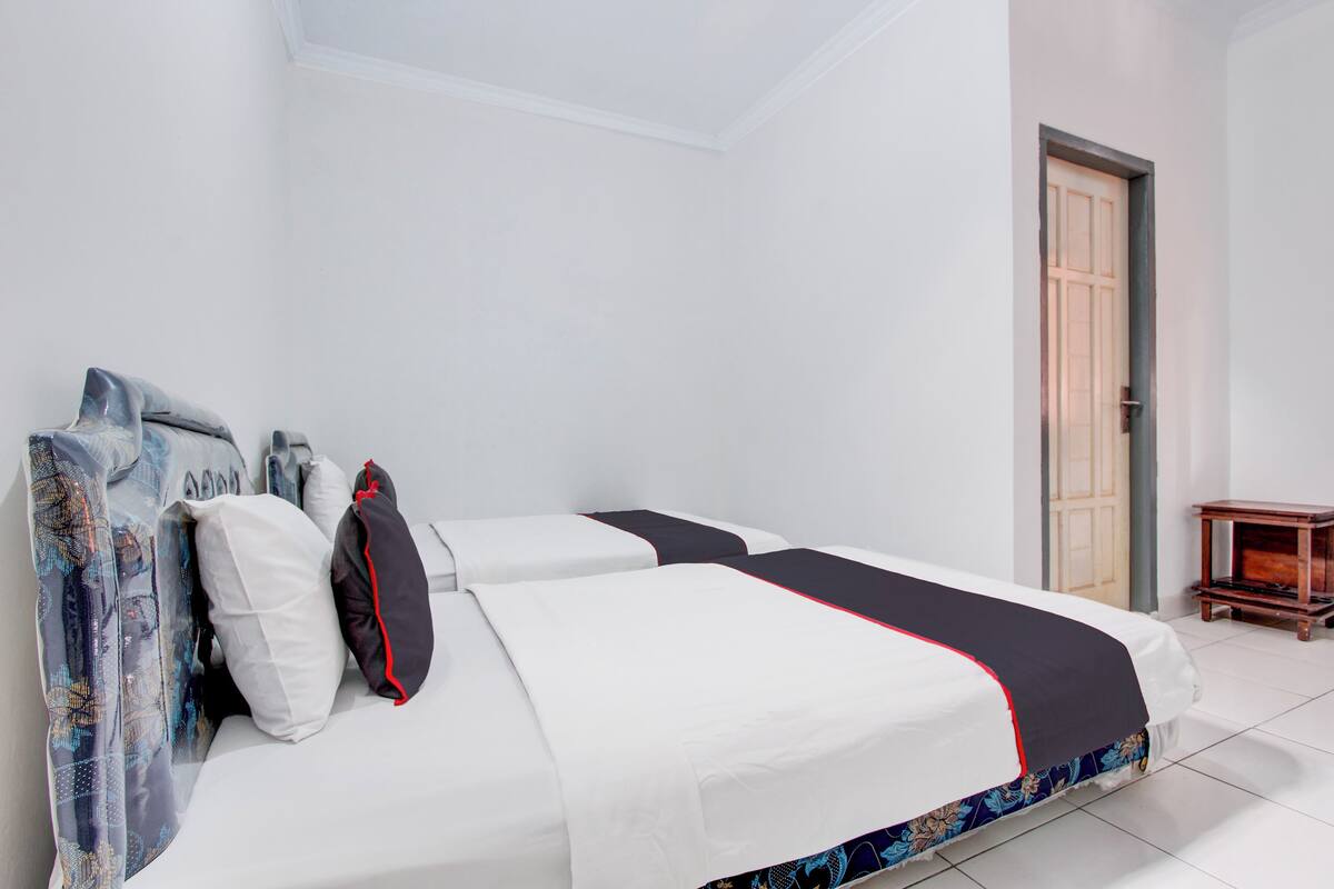 A neatly made bed with white bedding and a black and red accent, a wooden nightstand, and a door to the right.