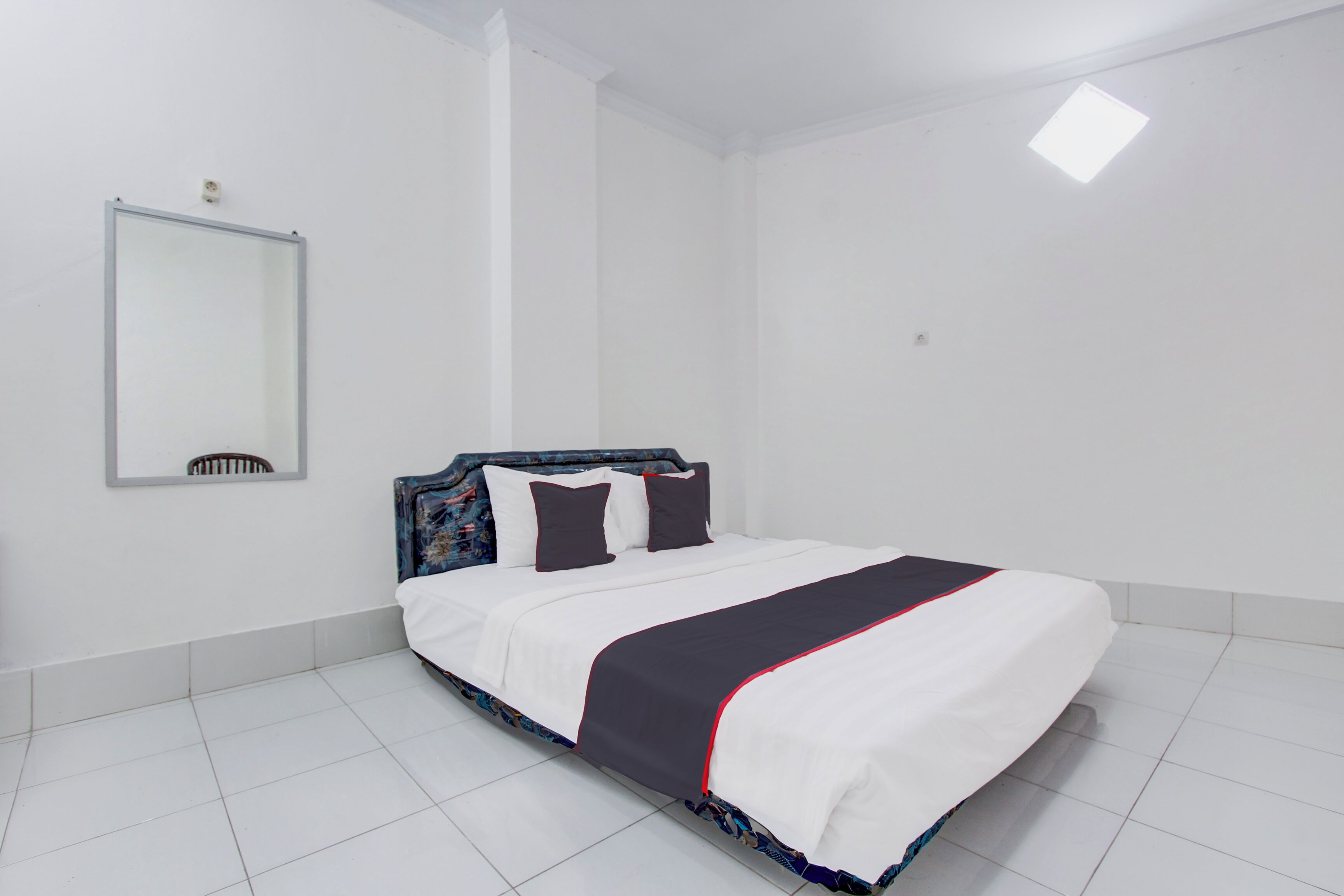 Una cama bien hecha con cabecera, paredes blancas y un espejo grande en la pared.