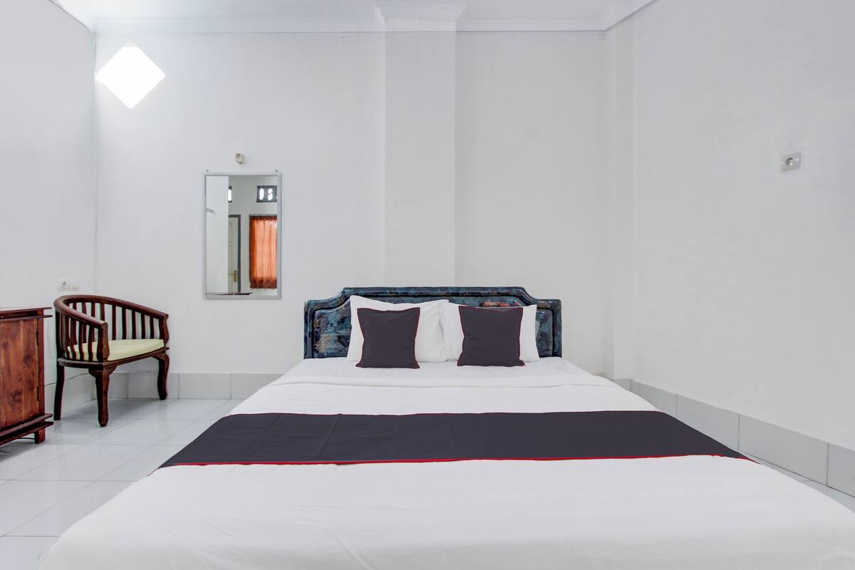 A neatly arranged bedroom with a bed, a wooden chair, a mirror, and a door.