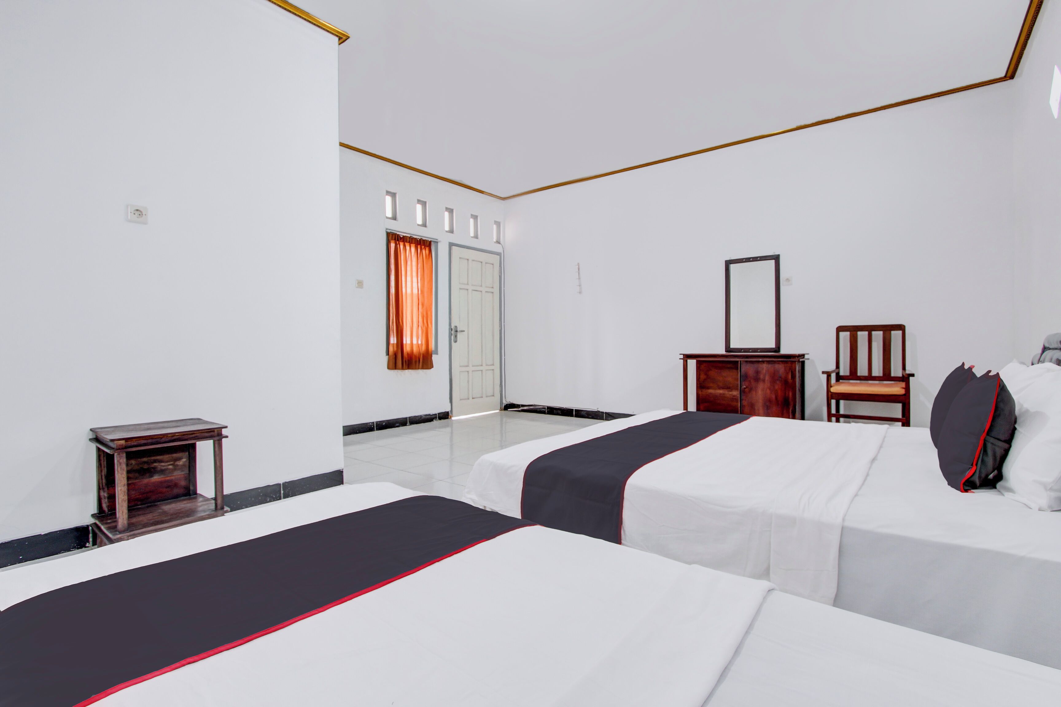 A hotel room with two beds, a wooden nightstand, a chair, a mirror, and a door with curtains.