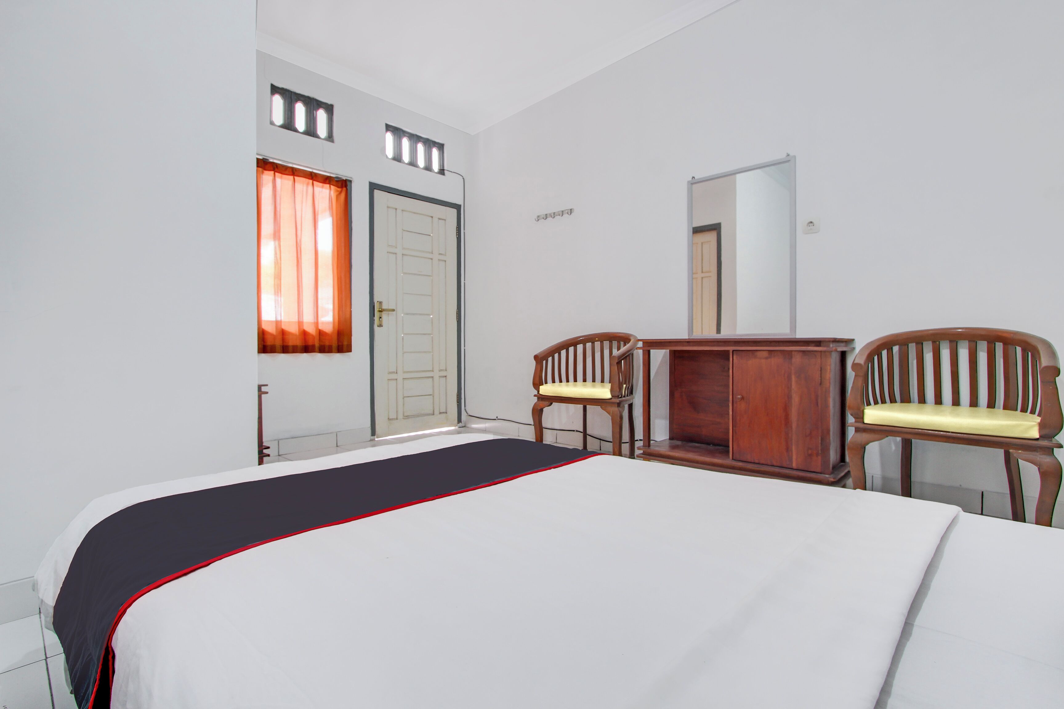 A hotel room with a bed, two wooden chairs, a wooden cabinet, a window with curtains, and a door.