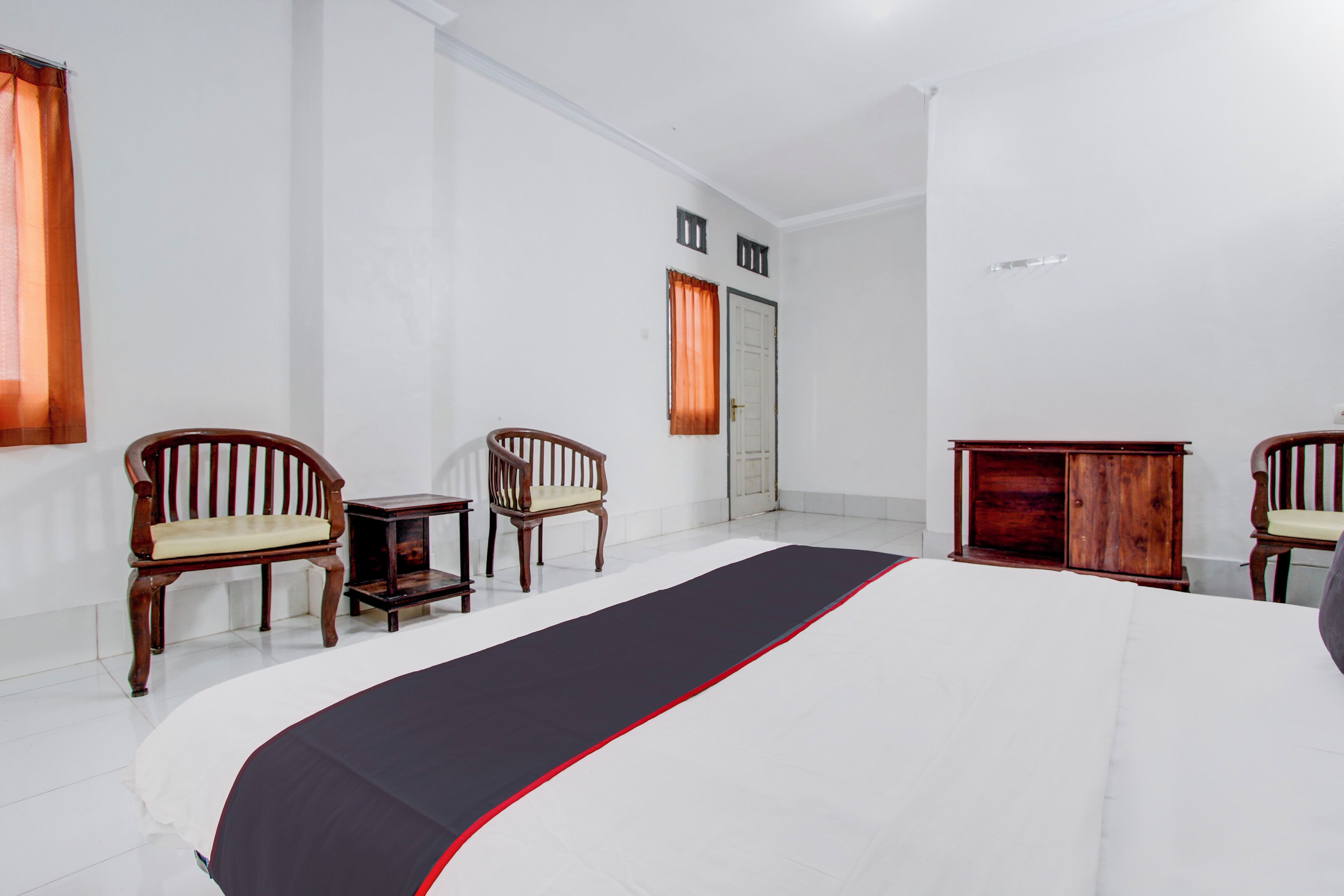 A hotel room with a large bed, two wooden chairs, a small table, and a cabinet.