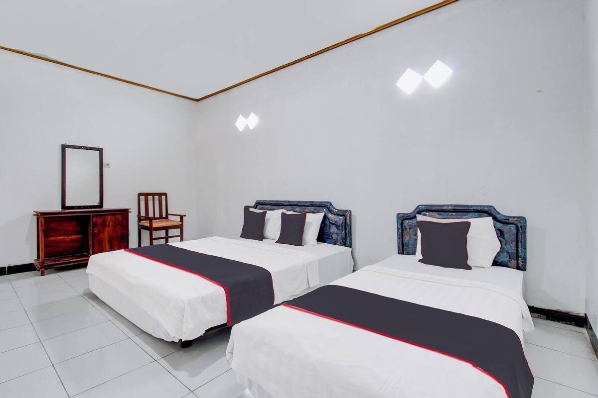 A hotel room with two beds, a wooden dresser, a chair, and a mirror.