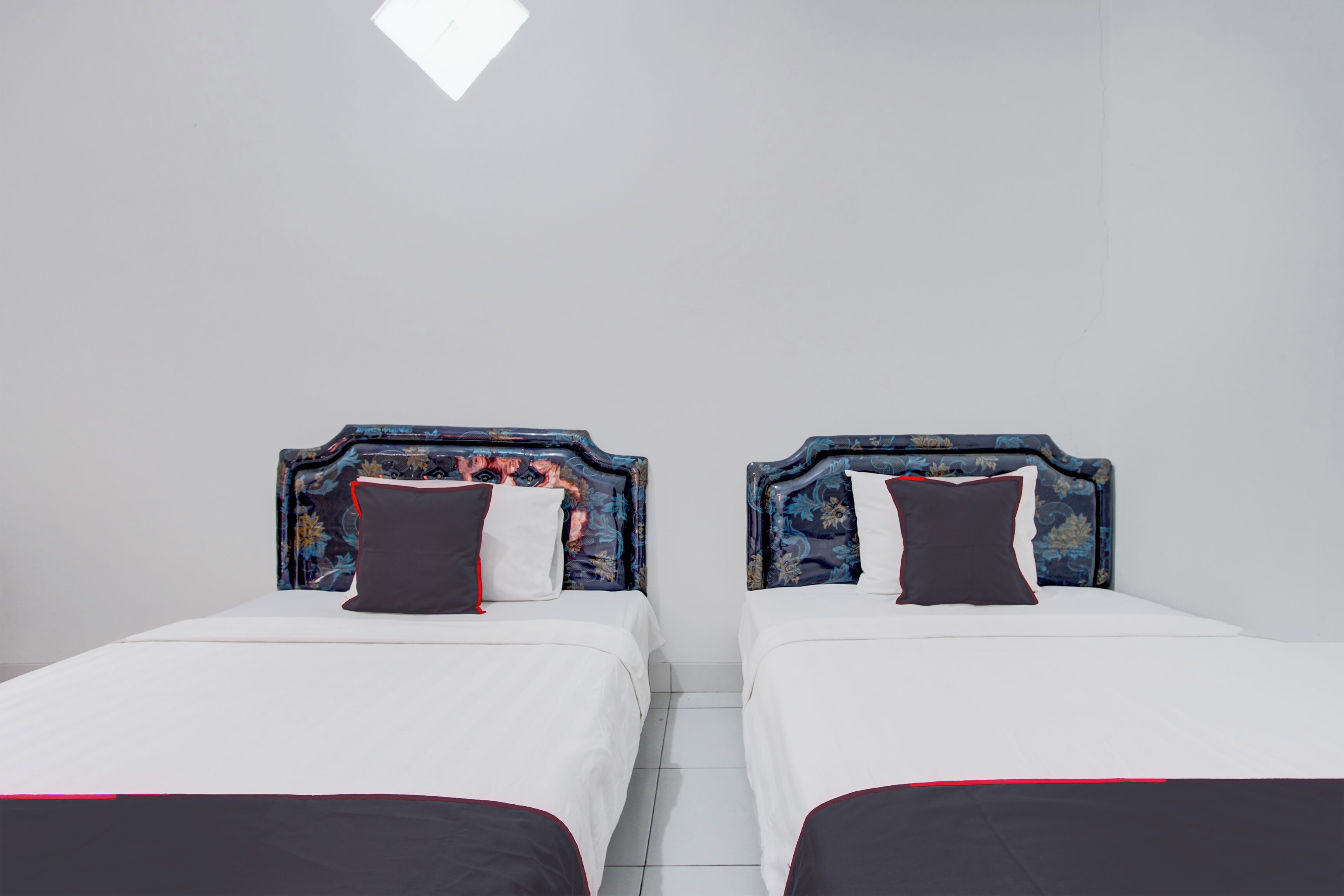 Twee bedden met bloemenmotieven op de hoofdborden en witte beddengoed in een kamer met witte wanden en een betegelde vloer.