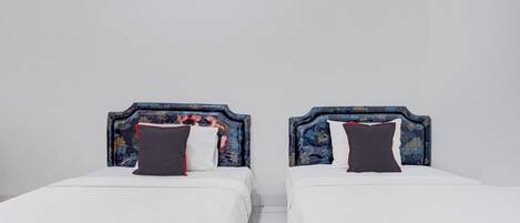 Twee bedden met bloemenmotieven op de hoofdborden en witte beddengoed in een kamer met witte wanden en een betegelde vloer.