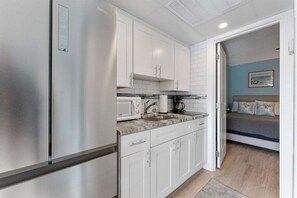 A compact kitchen with white cabinets, a stainless steel refrigerator, a microwave, and a sink.
