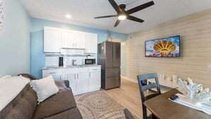 Un espacio habitable compacto con kitchenette, ventilador de techo, mesa de comedor y televisor montado en la pared.