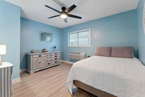 A bedroom with a bed, a dresser, a ceiling fan, a window with blinds, and an air conditioning unit.