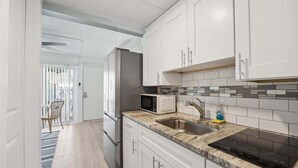 Une cuisine moderne avec des meubles blancs, un réfrigérateur en acier inoxydable, un four à micro-ondes et une plaque de cuisson à induction noire.