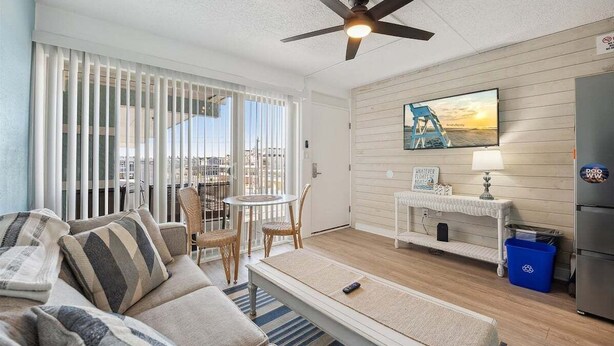 Un salon comprenant un canapé, une table basse, un téléviseur, un ventilateur de plafond et une vue sur la ville.