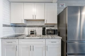 A modern kitchen with white cabinets, a stainless steel refrigerator, a microwave, and a sink with soap dispensers.