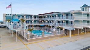 Um hotel com vários andares, piscina, área de estar externa e uma bandeira.