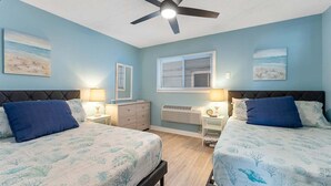 A bedroom with two beds, a ceiling fan, a window with blinds, and artwork on the walls.