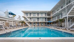 A swimming pool with lounge chairs and a multi-story building with balconies.