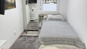 A small, well-lit bedroom with a bed, a desk, a chair, a TV, and a window with a view of buildings. - #3 Top room: central & comfortable, shared bathroom (Herne)