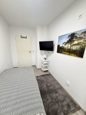 A bedroom with a bed, a television on a stand, a painting on the wall, and a door. - #3 Top Room: centrally located & comfortable, shared bathroom (Herne)