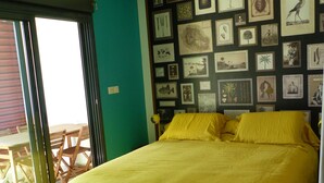A bedroom with a bed, a wall decorated with framed pictures, a window, and a door. - Attractive T2 apartment on the Saint Pierre waterfront in an ideally located building. (Saint-Pierre)