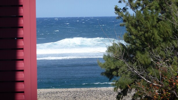 A beach view with waves, a red structure, and trees. - Attractive T2 apartment on the Saint Pierre waterfront in an ideally located building. (Saint-Pierre)