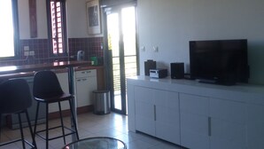 A modern kitchen with white cabinets, a dining area with a glass table, and a living room with a sofa and a TV. - Attractive T2 apartment on the Saint Pierre waterfront in an ideally located building. (Saint-Pierre)