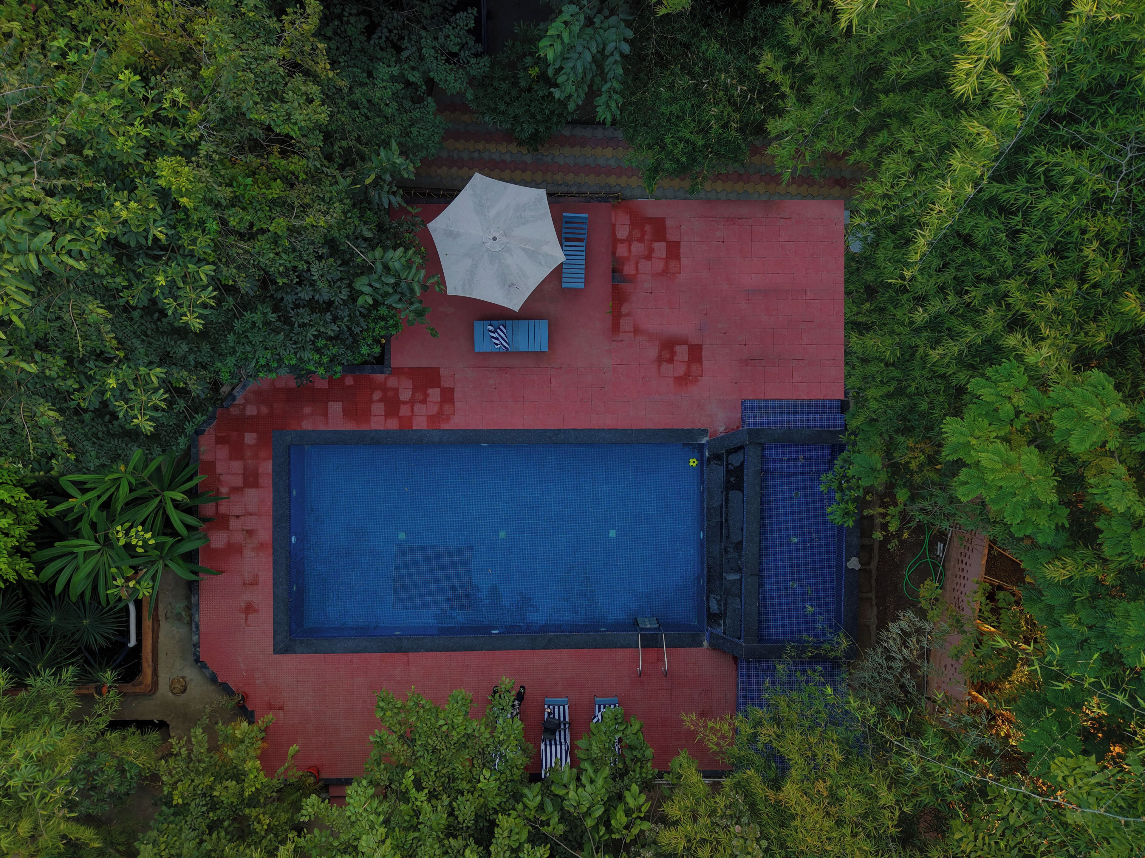 Vista aérea de una propiedad con piscina, un edificio rojo y vegetación circundante.