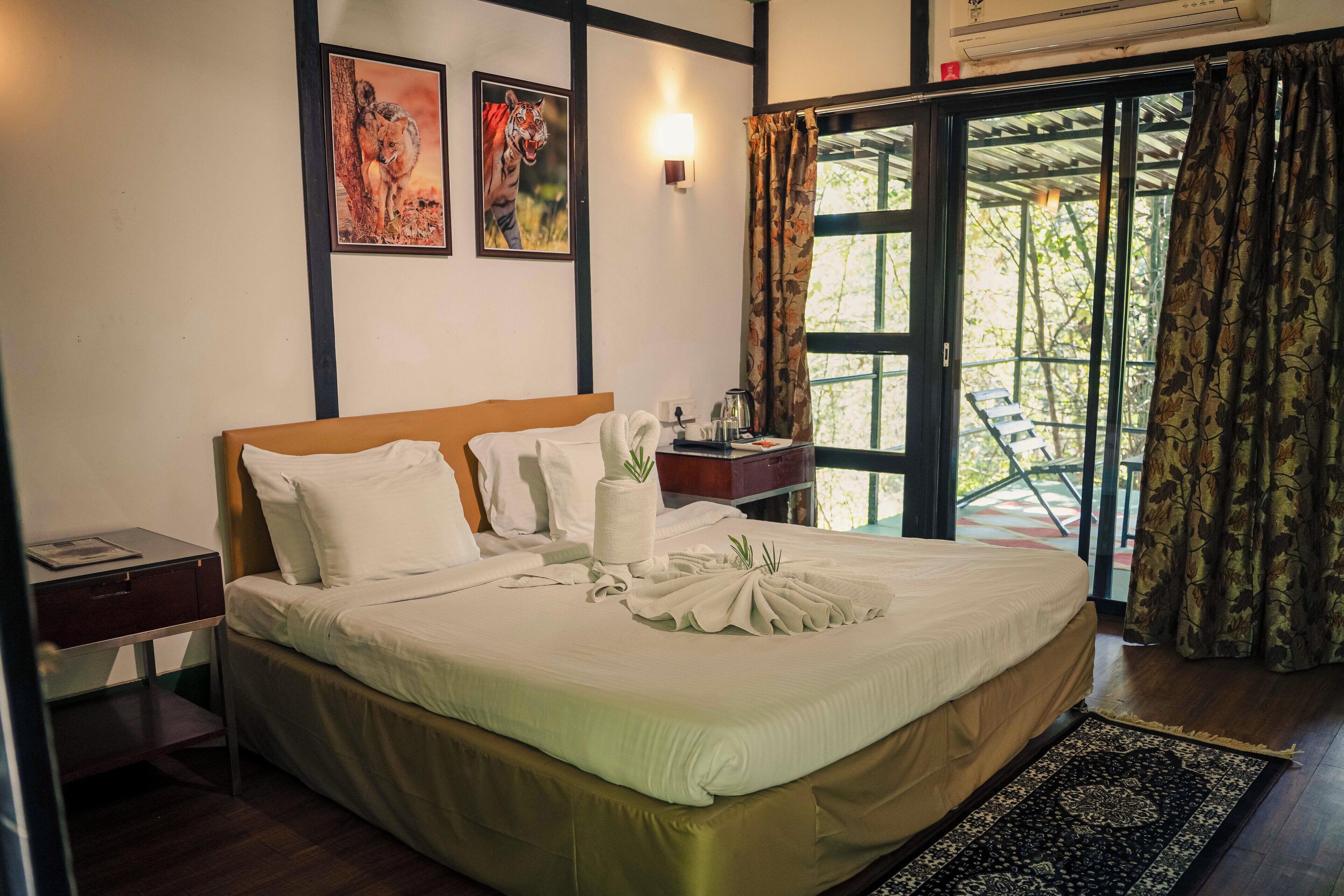 A neatly made bed with a towel and a decorative item on the bed, a nightstand with a lamp, and a window with curtains.