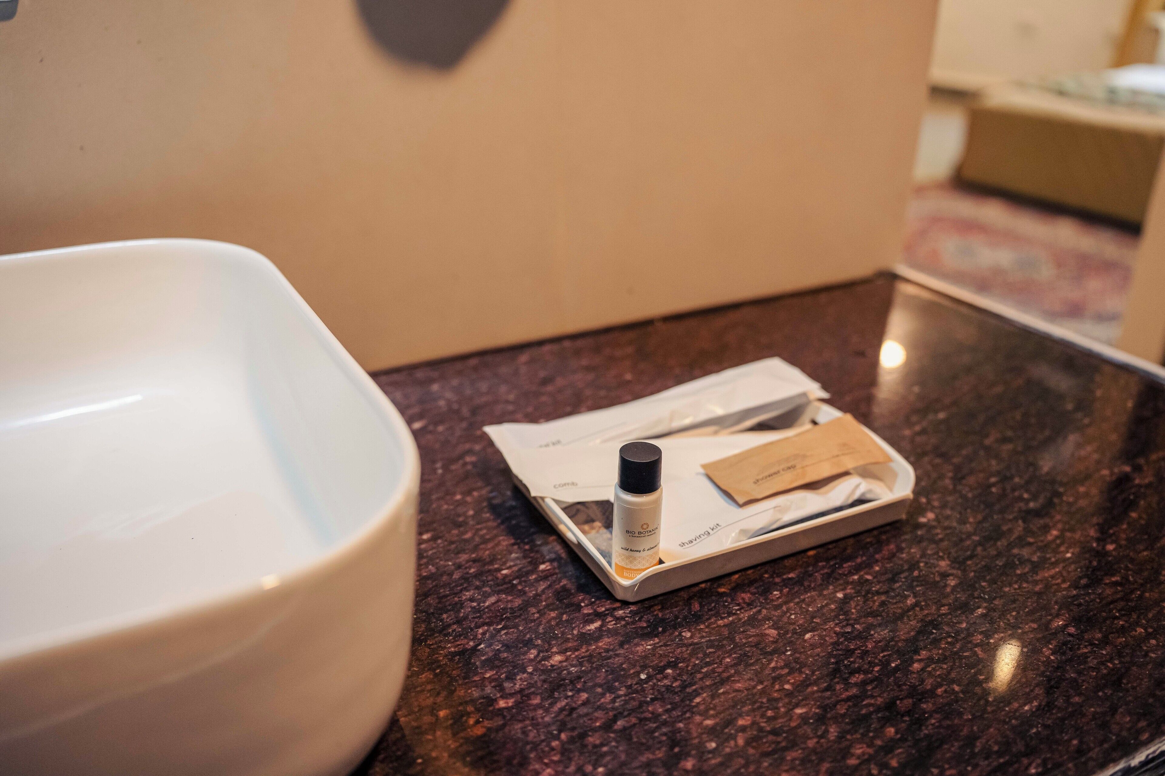 A bathroom counter with a white basin, a small bottle, and a tissue box.