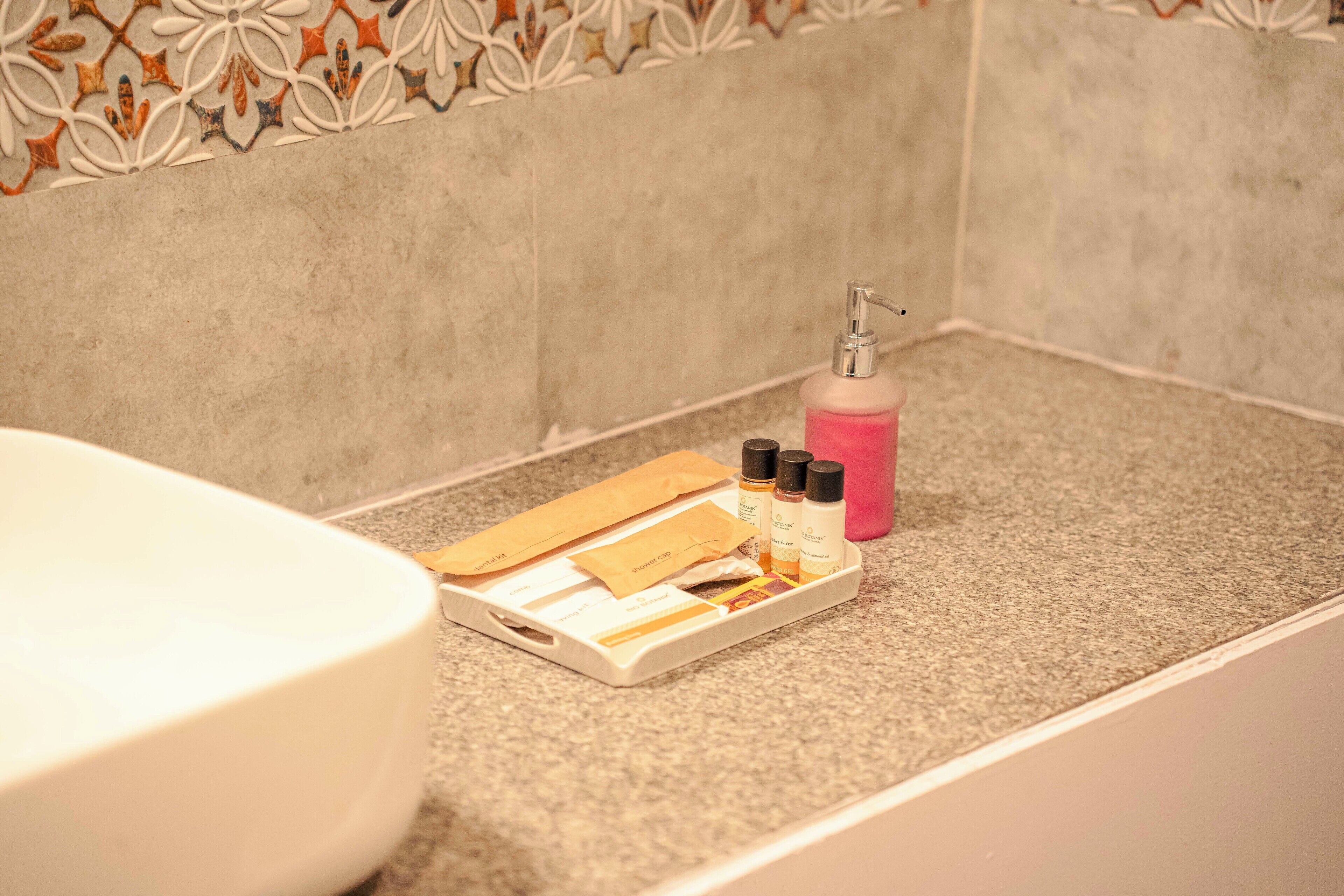 Een badkamer met een wit bad, een dienblad met toiletartikelen en een roze fles op het aanrecht.