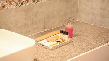Een badkamer met een wit bad, een dienblad met toiletartikelen en een roze fles op het aanrecht.