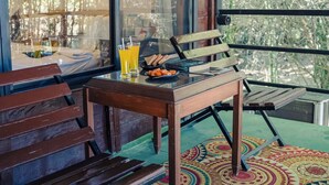 A wooden bench and table with a colorful rug, a glass window, and a view of trees outside. - Wilderness camp Resort Pench (Kurai)