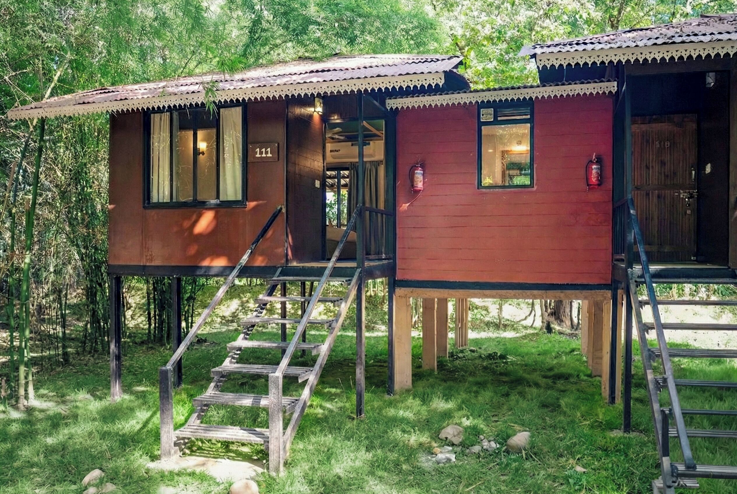 Dos cabañas de madera con escaleras exteriores, numeradas 111 y 112, ubicadas en una zona boscosa.