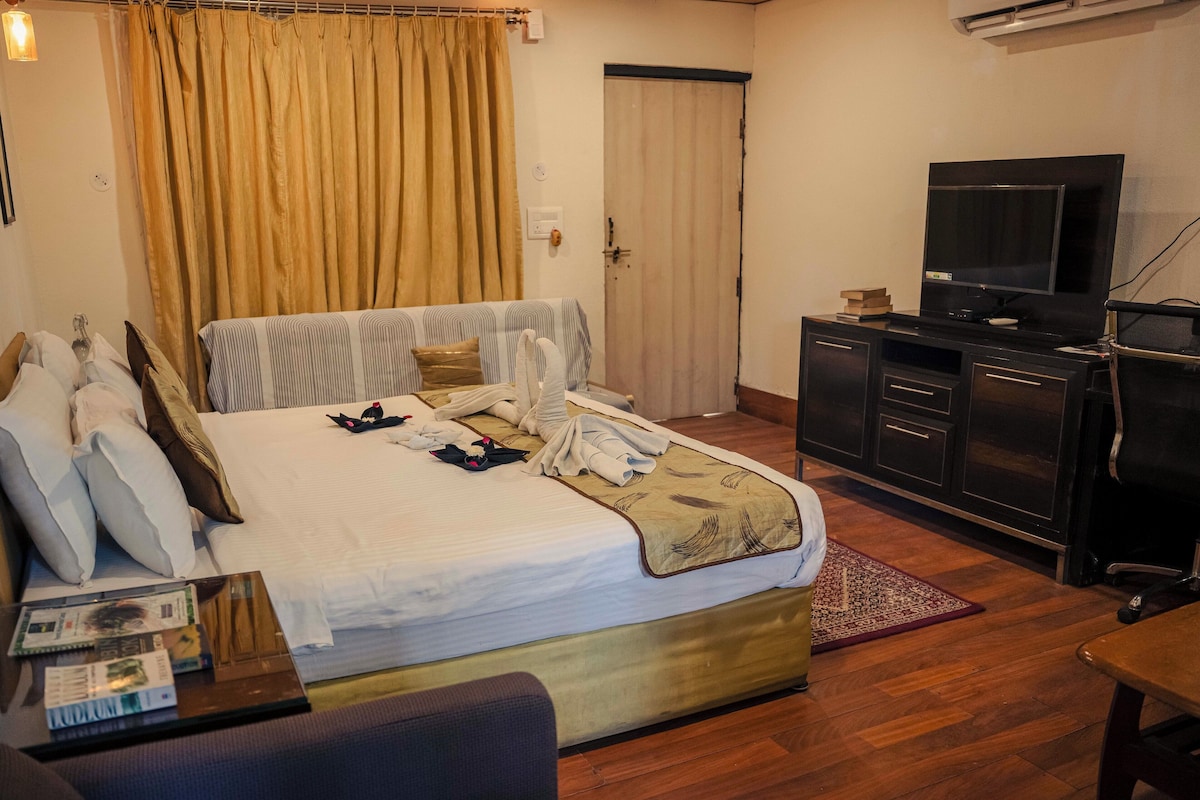 A hotel room with a large bed, a television, a desk, and a wardrobe.