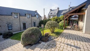 A stone building with a paved driveway, a wooden pergola, and bicycles parked under it. - Large, bright renovated farmhouse (Étel)