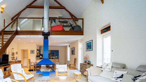 A spacious living area with a high ceiling, a wooden staircase, a dining table, and a sofa. - Large, bright renovated farmhouse (Étel)