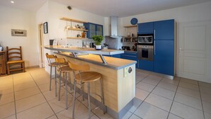 A modern kitchen with a central island, bar stools, blue cabinets, and stainless steel appliances. - Large, bright renovated farmhouse (Étel)
