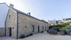 A stone building with a courtyard, featuring a paved walkway and potted plants. - Large, bright renovated farmhouse (Étel)
