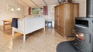 A cozy cabin interior with a sofa, a wooden table, a cabinet, and a wood-burning stove.