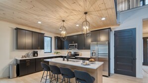A modern kitchen with dark cabinets, stainless steel appliances, and a central island with bar stools. - Indoor Pool, Hot Tub, Firepit, Theater | All-Season Retreat | Kings Crown (Gatlinburg)