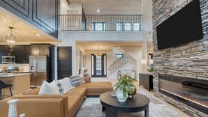 A spacious living area with a large sofa, a coffee table, and a fireplace. There is a kitchen area with modern appliances and a dining table. - Indoor Pool, Hot Tub, Firepit, Theater | All-Season Retreat | Kings Crown (Gatlinburg)
