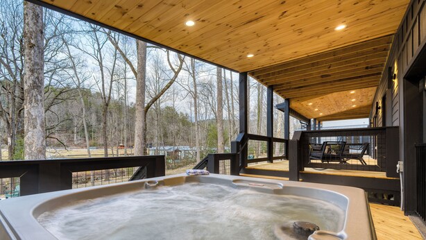 A hot tub in a wooden deck area with a view of trees and a building in the background. - Indoor Pool, Hot Tub, Firepit, Theater | All-Season Retreat | Kings Crown (Gatlinburg)