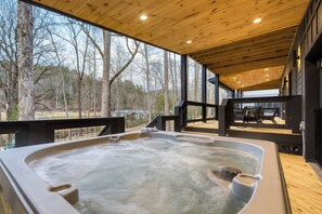 A hot tub in a wooden deck area with a view of trees and a building in the background. - Indoor Pool, Hot Tub, Firepit, Theater | All-Season Retreat | Kings Crown (Gatlinburg)